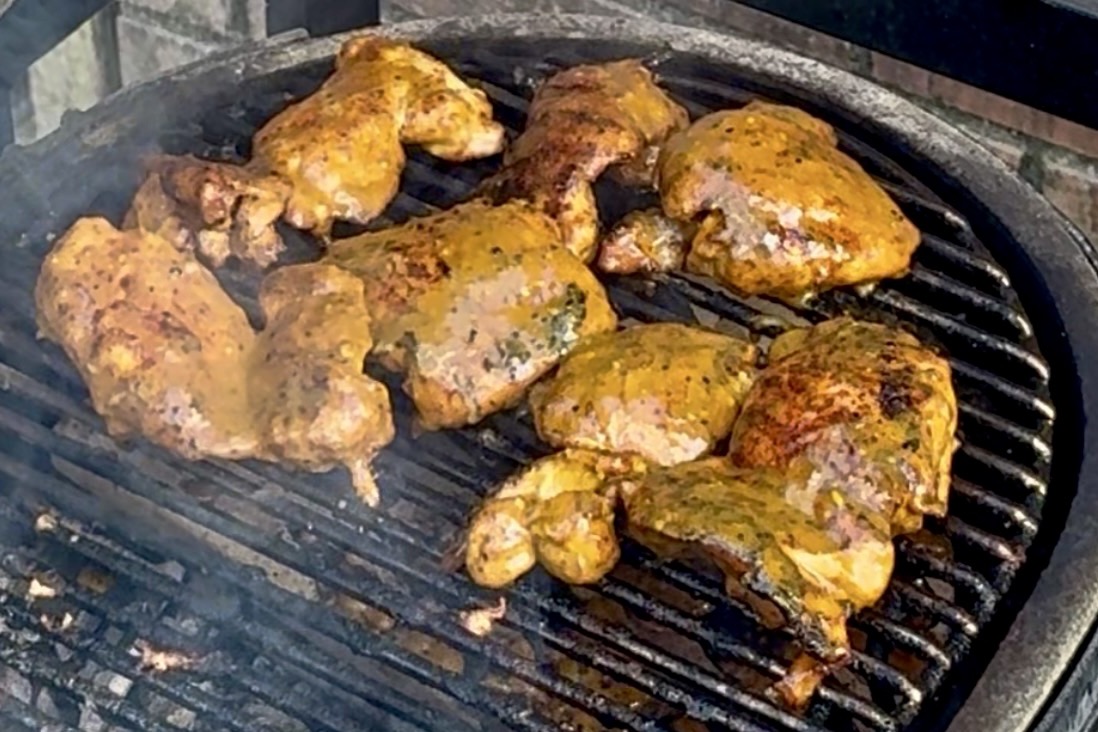 Several pieces of seasoned chicken cooking on a grill grate.