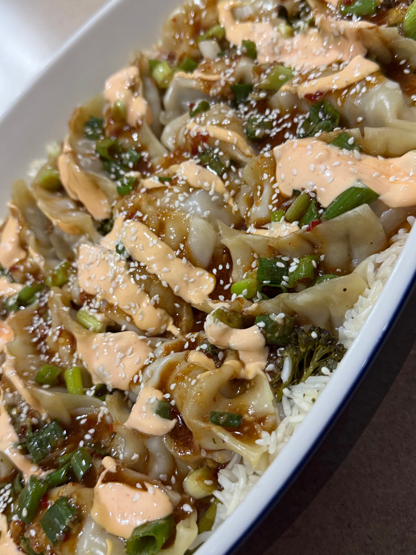 Dumplings served over white rice, drizzled with a creamy sauce and topped with sesame seeds and chopped green onions.