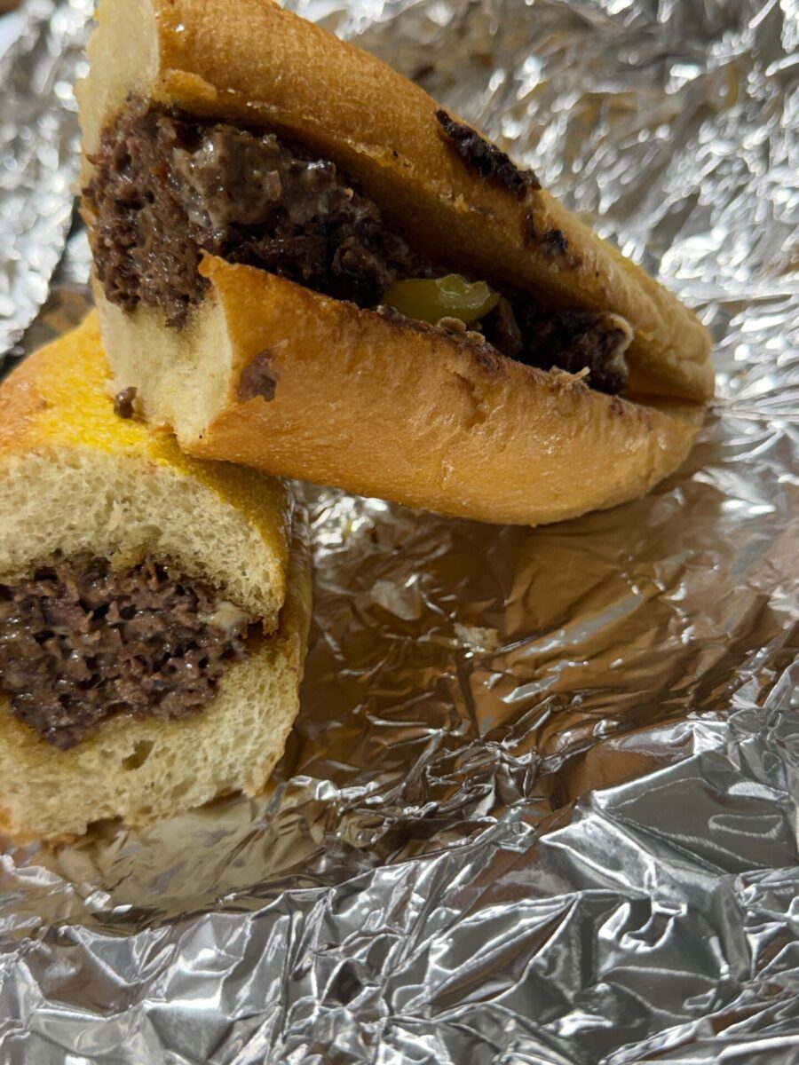 A cheesesteak sandwich cut in half, served on aluminum foil.