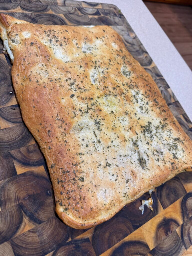 A rectangular, golden-brown flatbread seasoned with dried herbs on a wooden cutting board.