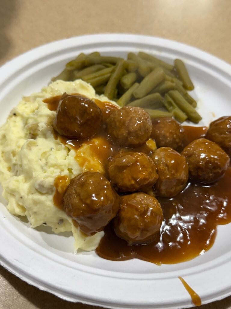 A plate of meatballs in brown gravy served with mashed potatoes and green beans.
