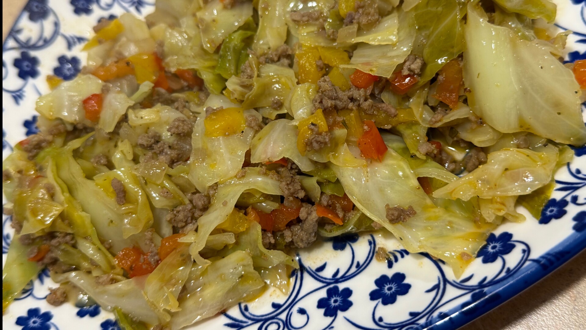 A stir-fry of cabbage, ground meat, and bell peppers served on a plate with a blue floral pattern.