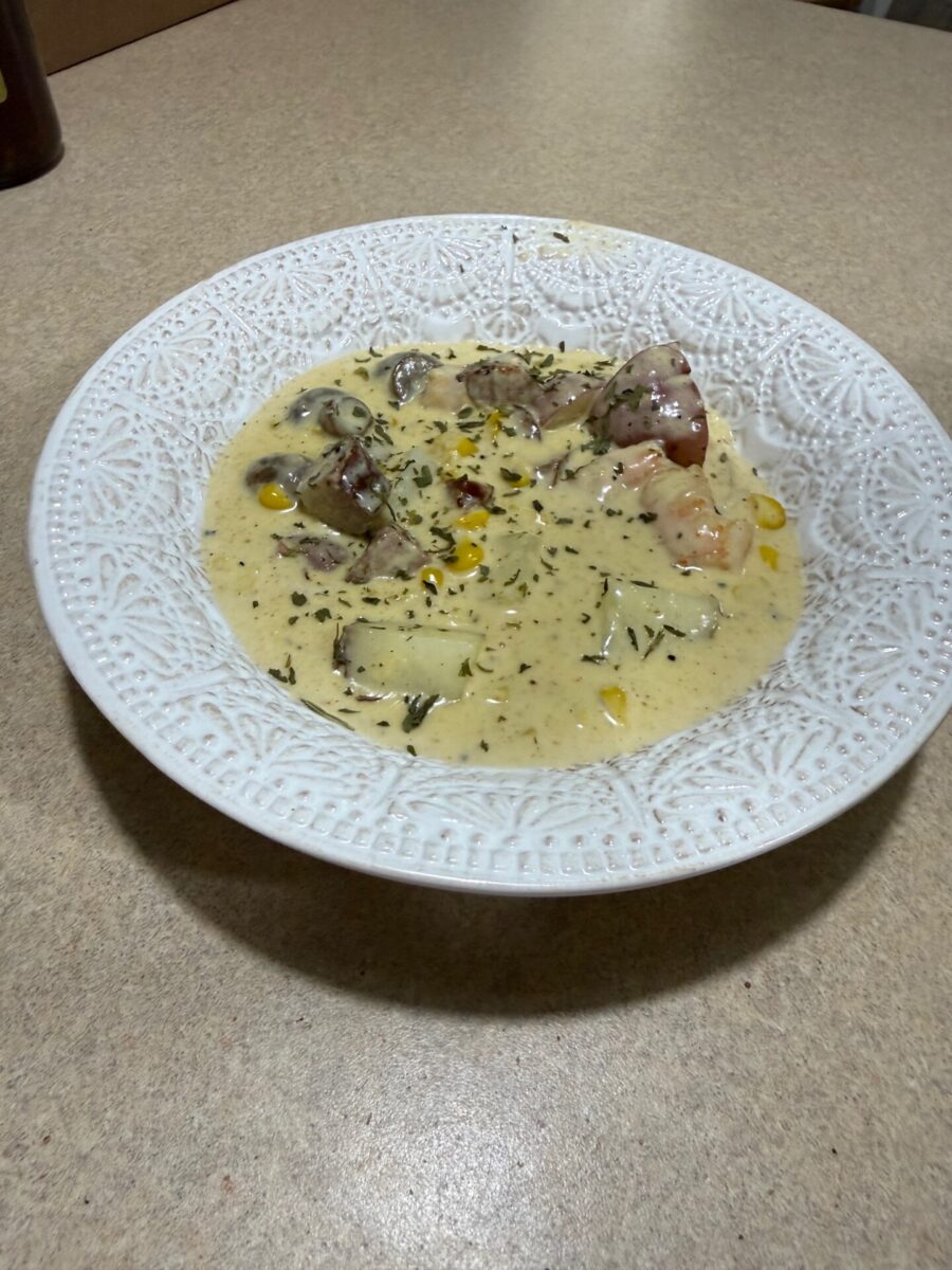 A bowl of creamy potato and corn chowder garnished with dried herbs in a white, ornate bowl.