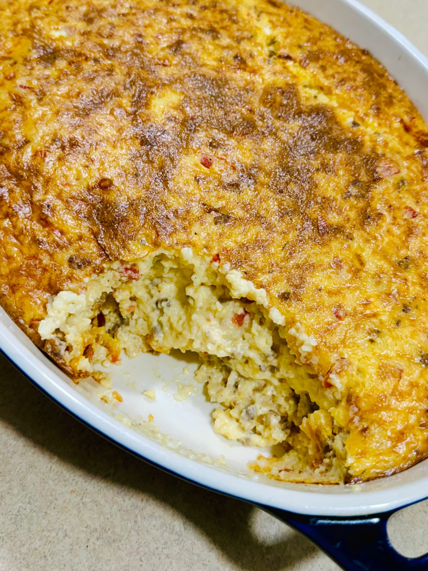 A baked cheesy casserole with a golden-brown crust and a large scoop removed from the center.