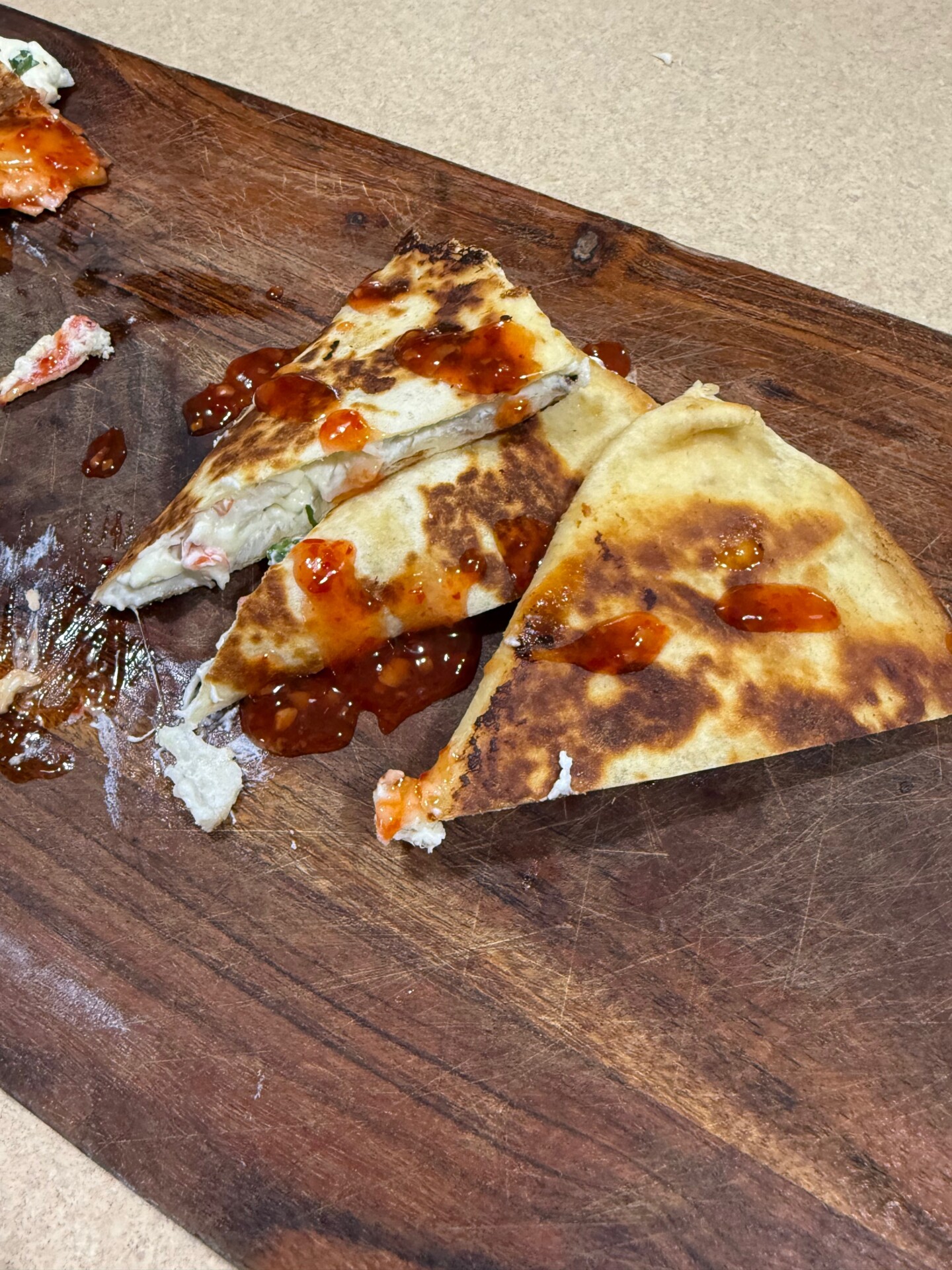 Triangular quesadilla wedges drizzled with red chili sauce on a wooden cutting board.