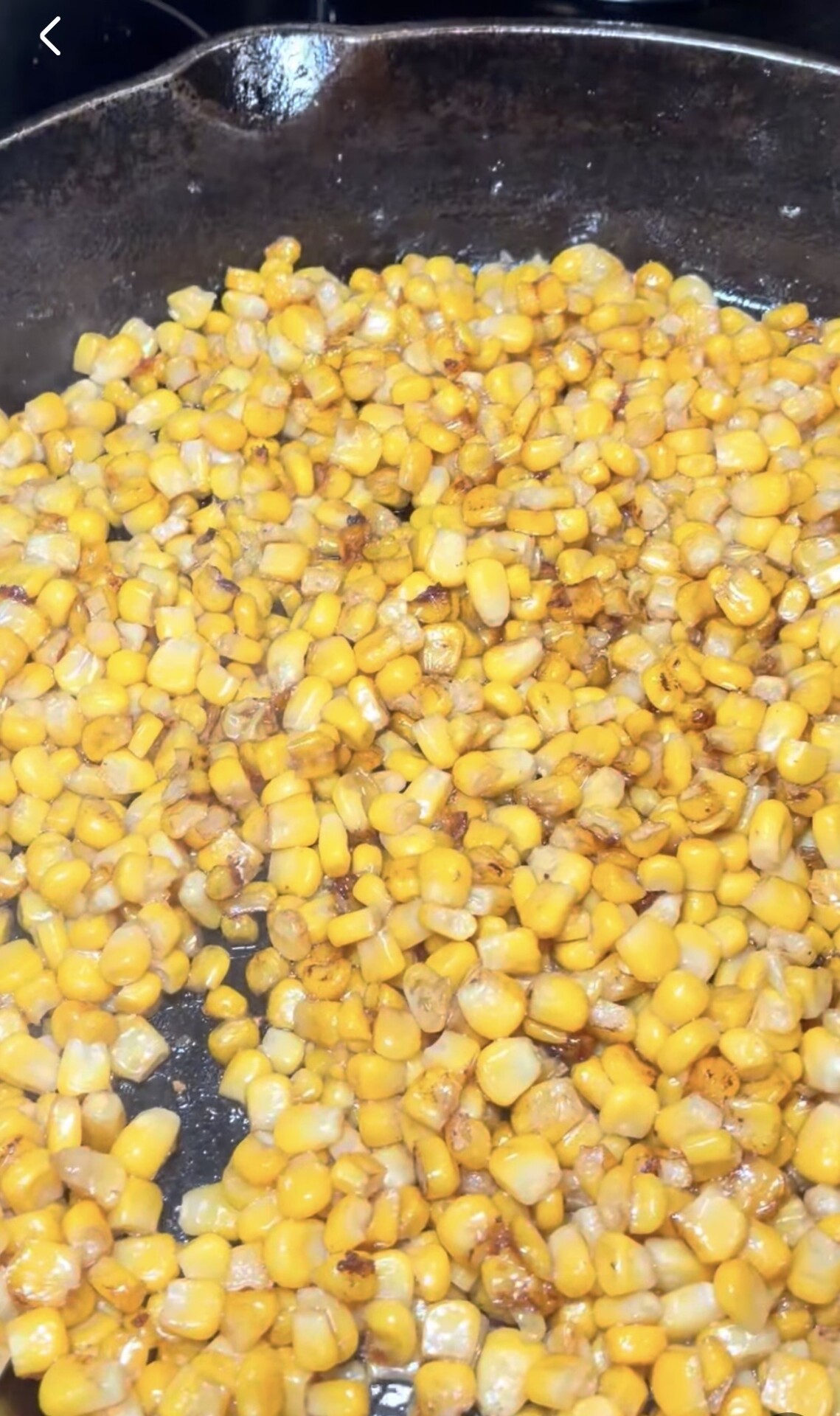 Yellow corn kernels searing in a cast iron skillet.
