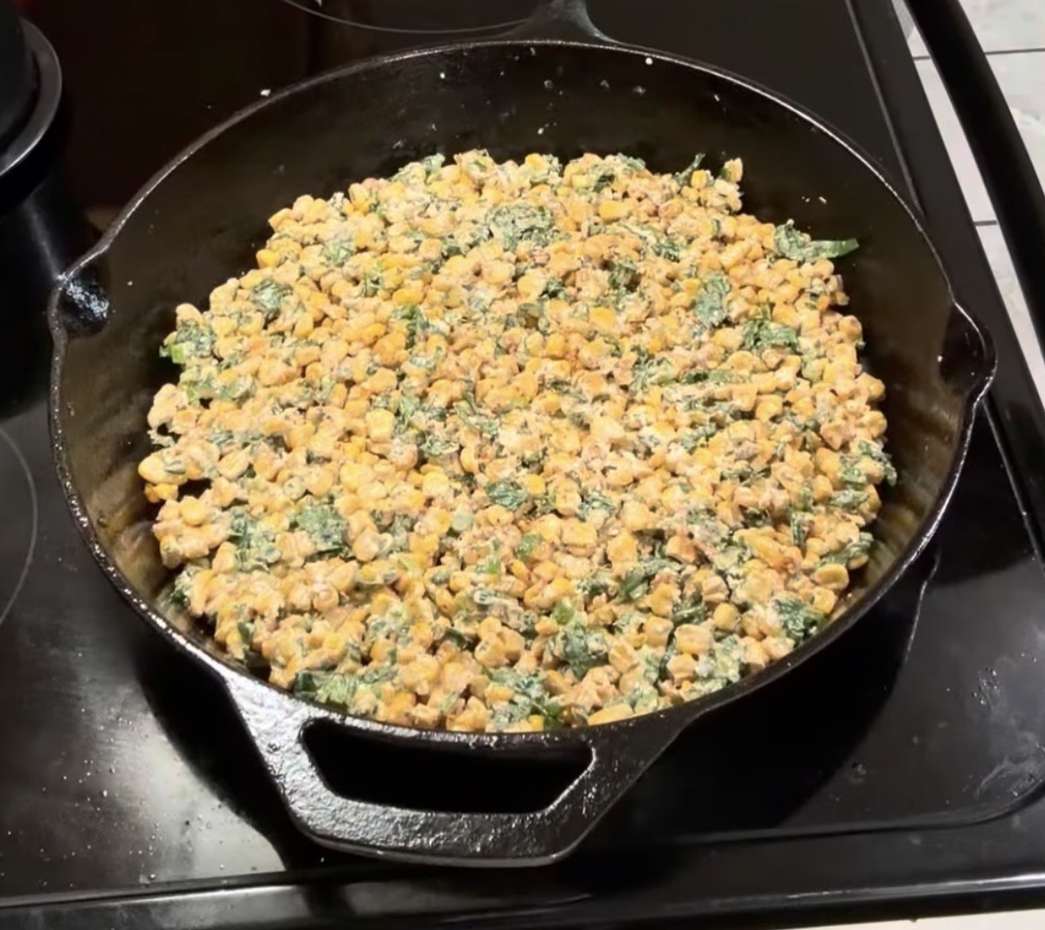 A cast iron skillet filled with a mixture of corn, greens, and a creamy sauce.