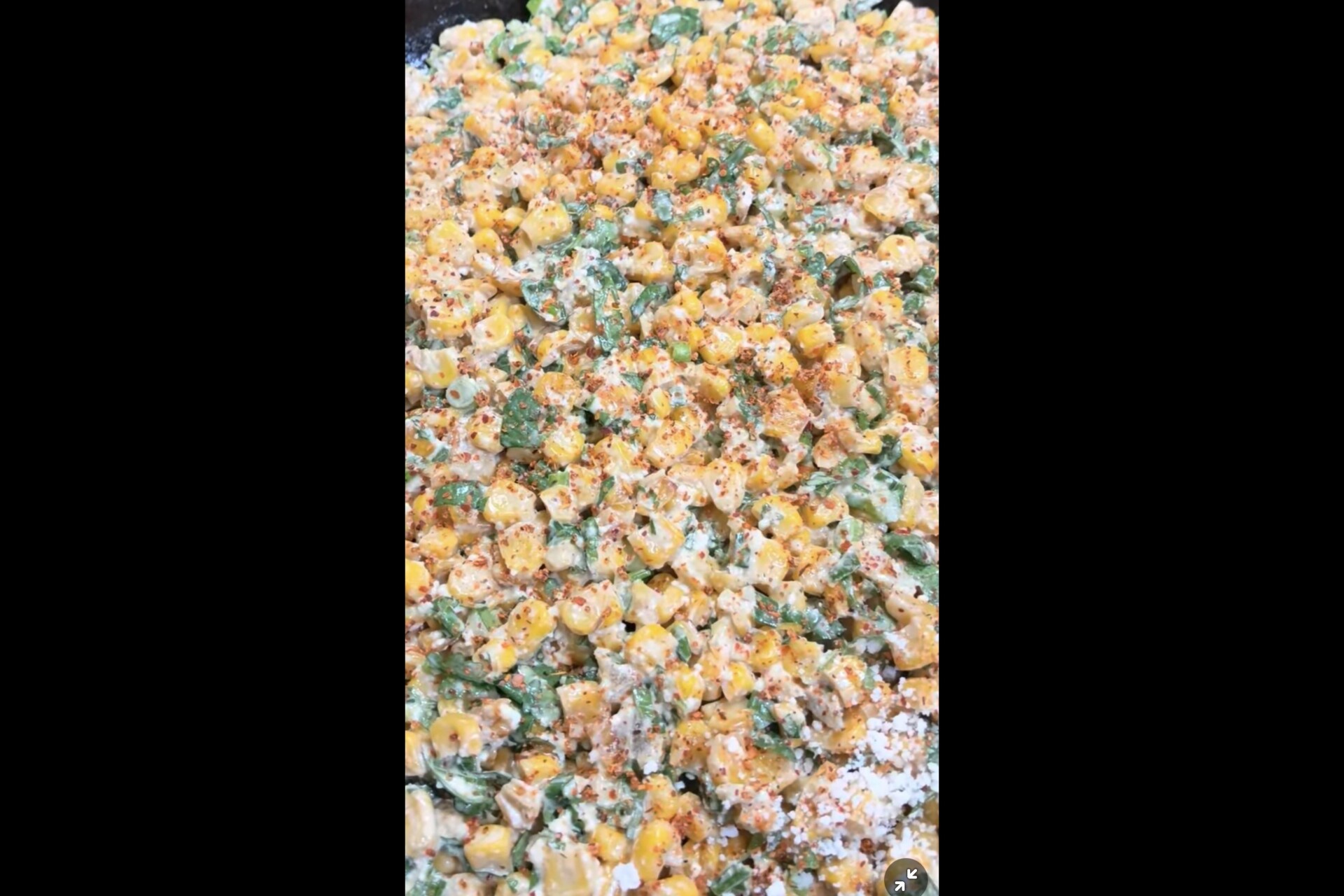 A skillet of Mexican street corn salad topped with herbs, chili powder, and crumbled cheese.