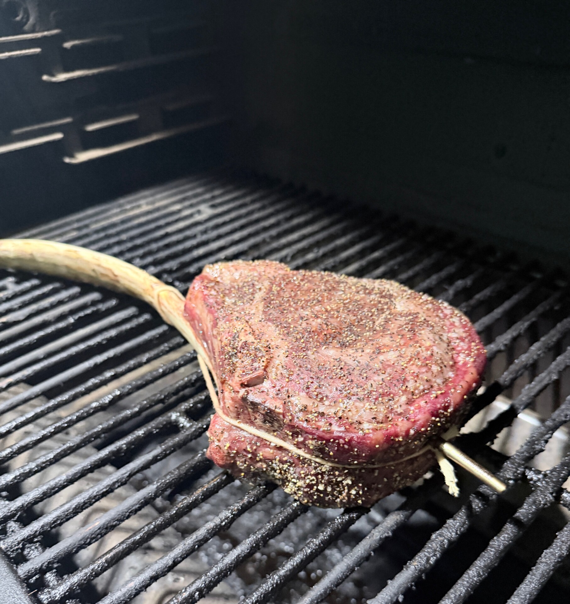 A seasoned tomahawk steak cooking on a grill grate.