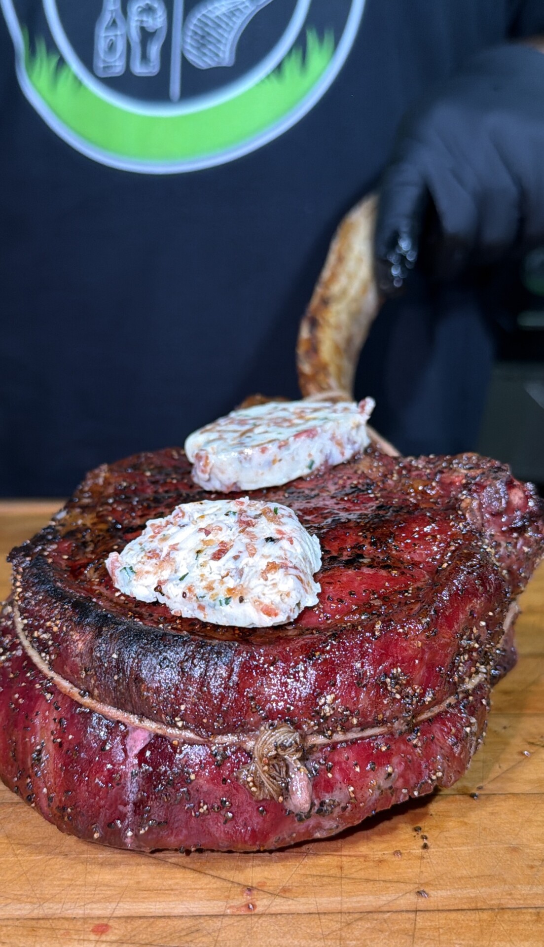 A thick, seared tomahawk steak topped with two pats of herb butter, resting on a wooden cutting board.