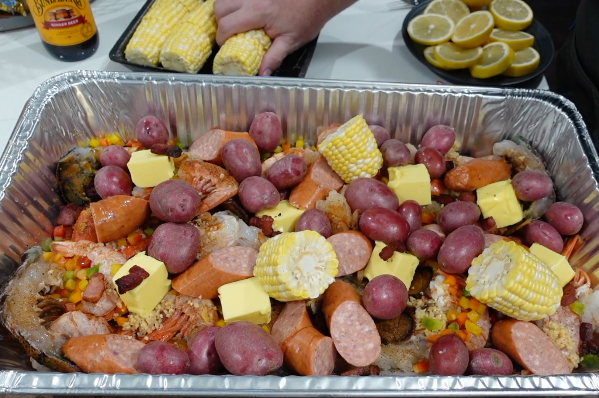 Large aluminum pan filled with a shrimp boil containing red potatoes, corn on the cob, sliced sausage, and cubes of butter.