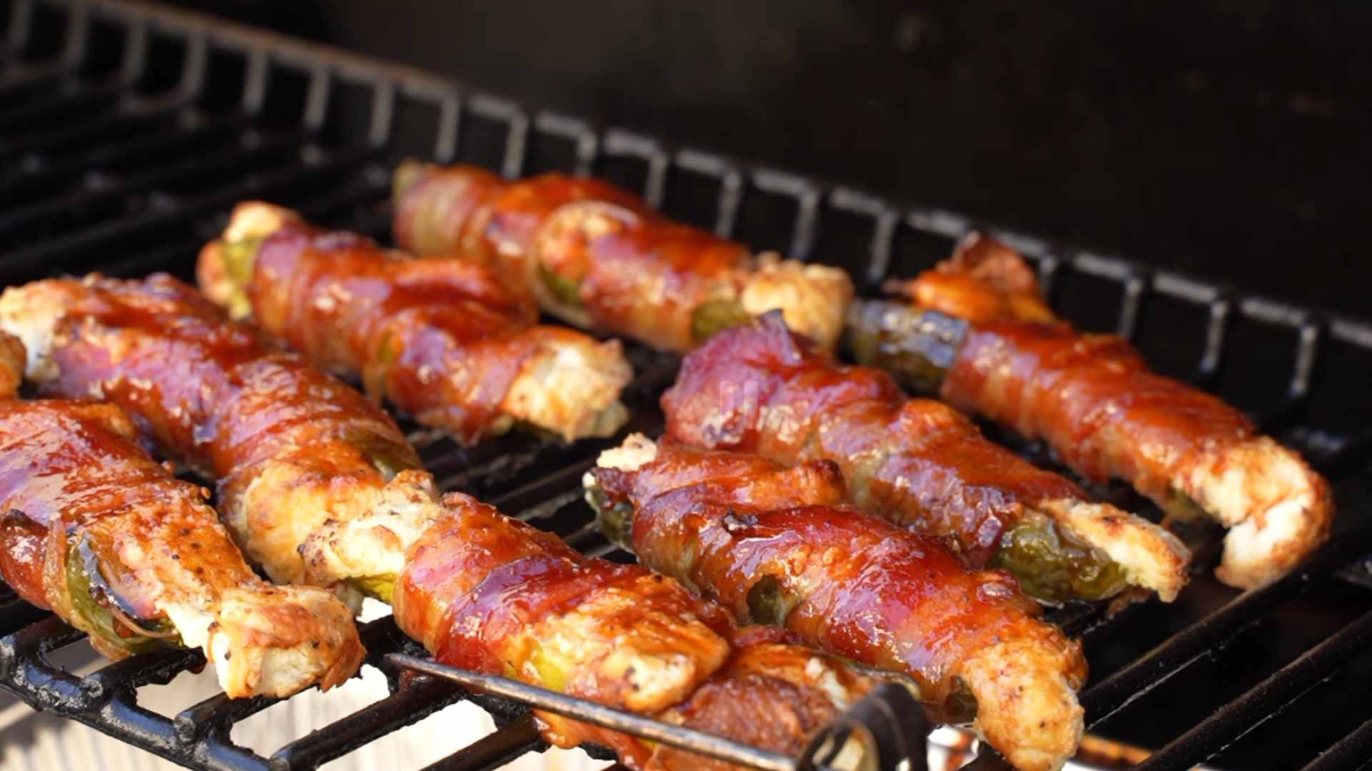 Bacon-wrapped jalapeño poppers grilling on a barbecue rack.